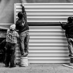 grayscale photo of three men arranging metal wall